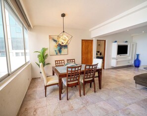 A dining area with a wooden table and chairs, a hanging light fixture, a painting on the wall, and a TV mounted on the wall. - Da Vinci Suites best location in Condado (San Juan)