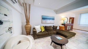 Uma sala de estar moderna com um sofá seccional, uma mesa de centro redonda e um quadro grande na parede.