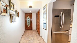 Um corredor com porta de madeira, geladeira e espelhos emoldurados na parede.