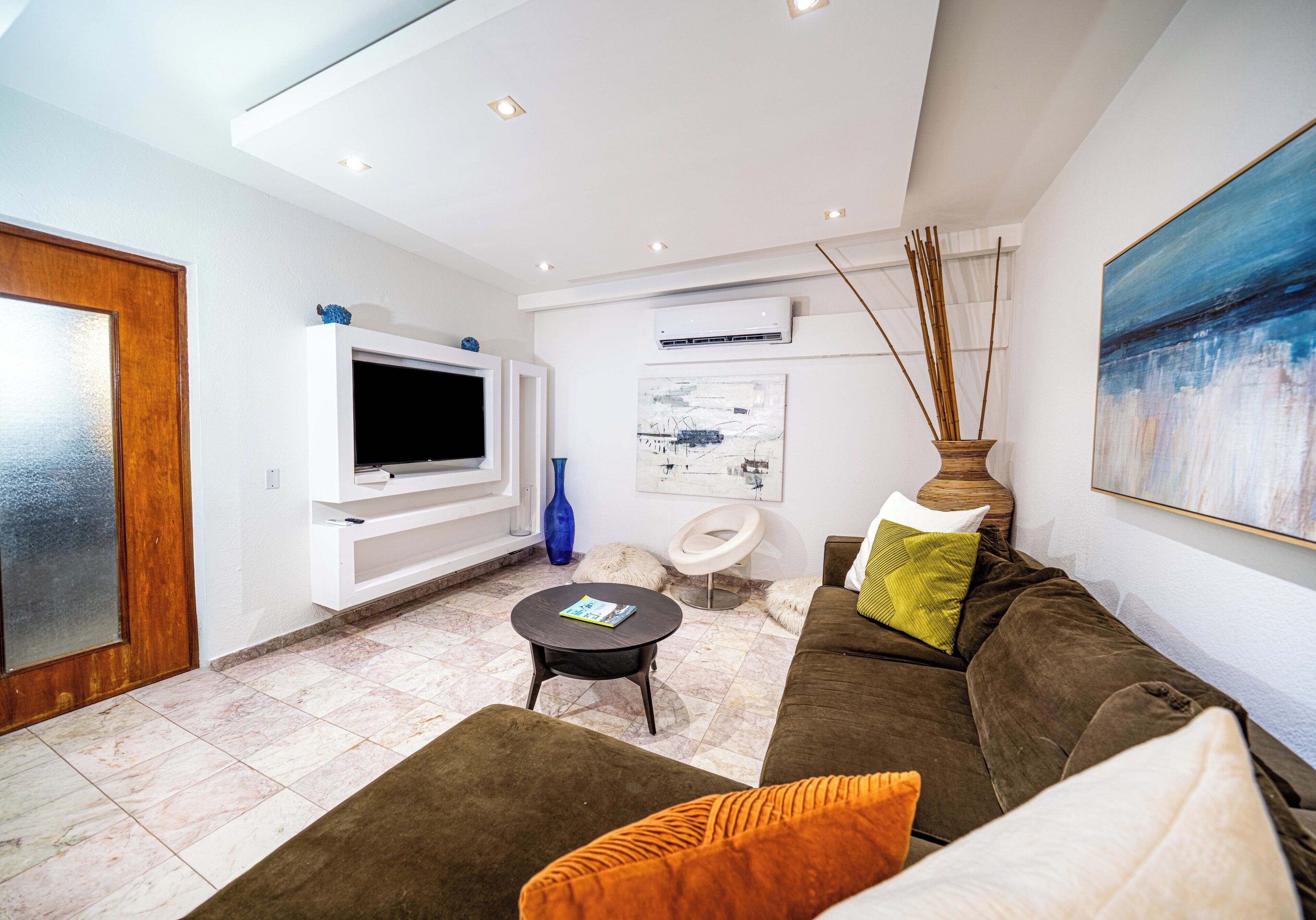 A modern living room with a flat-screen TV, a sofa, a coffee table, and a painting on the wall.