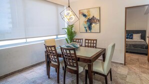 Uma área de refeições com mesa, cadeiras, luminária pendente, planta em vaso e um quadro na parede.