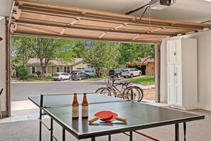 Ein Tischtennistisch mit zwei Flaschen und Schlägern in einer Garage, mit Blick auf eine Wohnstraße.