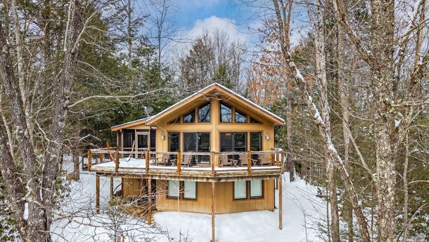 Una cabaña de madera con balcón, rodeada de árboles nevados.