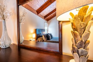 Una camera da letto con soffitto in legno, un letto con testiera, un comodino, una lampada e un vaso con fiori.