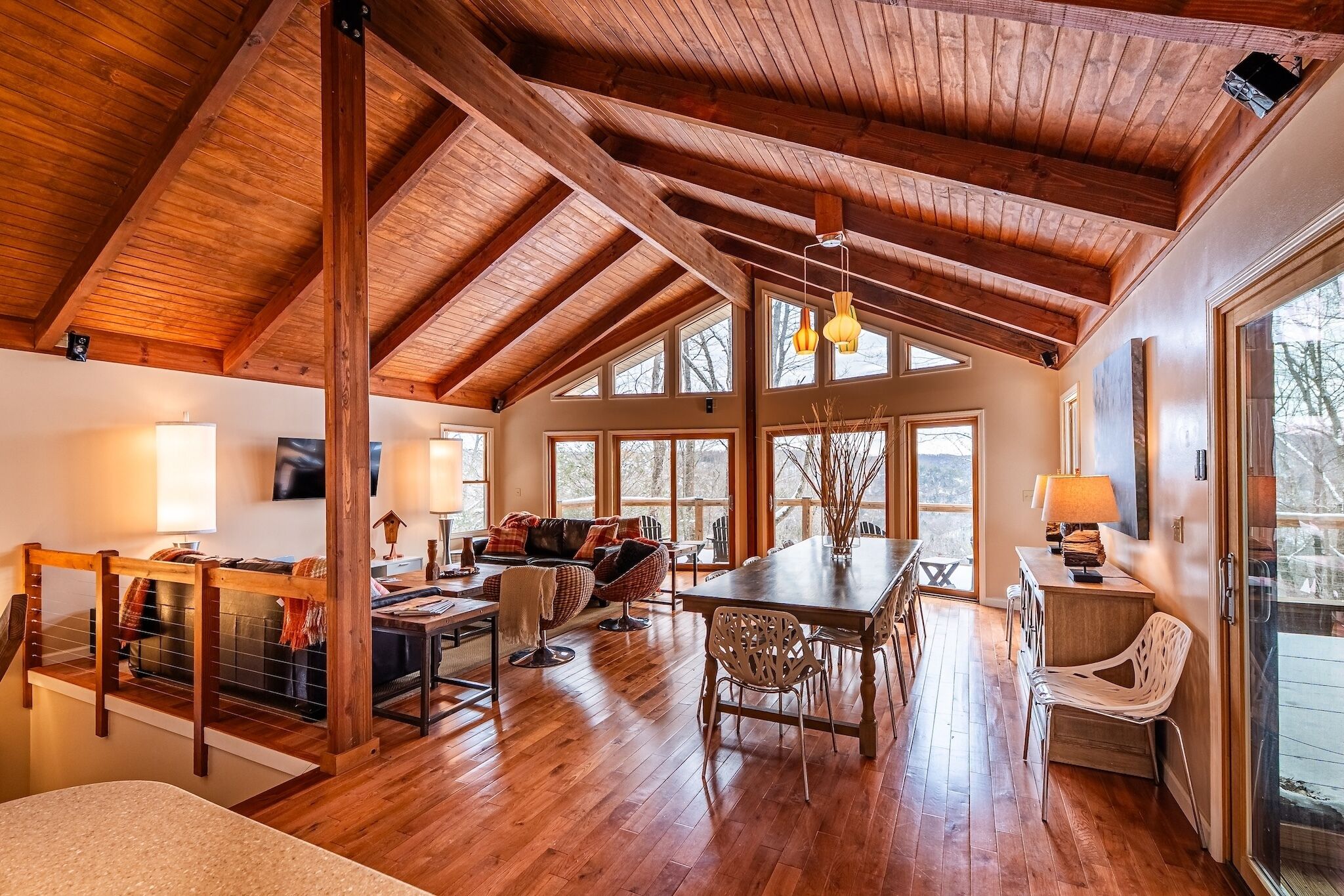 A spacious room with a high wooden ceiling, large windows, and a dining area with a table and chairs.