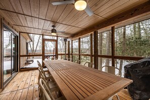 A wooden deck with a long table and chairs, large windows, and a ceiling fan. - Luxury home on The Meadow River with stunning view of the river canyon (Hico)