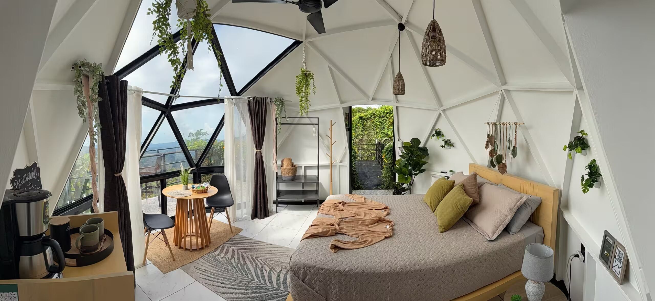 Une chambre moderne et spacieuse, dotée d’un grand lit, d’un coin salon avec une table et offrant une vue sur la verdure environnante.