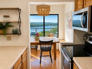 A kitchen with a view of a lake, a dining area with a table and chairs, and a hanging light fixture. - Charming 4BR Lakefront Condo Getaway- Near Boat Marina and Silver Dollar City. (Branson)