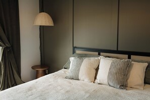 Ein Bett mit einer strukturierten weißen Bettdecke, einem Kopfteil mit gewebtem Muster und einem kleinen Nachttisch mit Lampe.