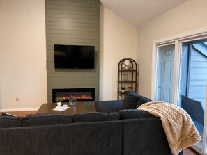 A living room with a sectional sofa, a flat-screen TV, a fireplace, and a bookshelf. - Charming 4BR Lakefront Condo Getaway- Near Boat Marina and Silver Dollar City. (Branson)