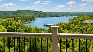 A scenic view of a lake surrounded by lush greenery, with a dock and a house visible in the foreground. - Charming 4BR Lakefront Condo Getaway- Near Boat Marina and Silver Dollar City. (Branson)
