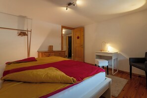 Ein Schlafzimmer mit Bett, Schreibtisch, Stuhl und einer Tür zu einem anderen Raum.