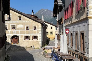 Eine enge Straße mit traditionellen Gebäuden, ein Berg im Hintergrund und eine Schweizer Flagge.