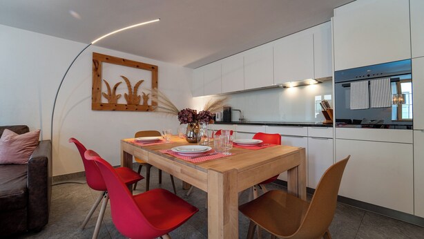 Eine moderne Küche mit weißen Schränken, einem Holztisch und roten Stühlen.