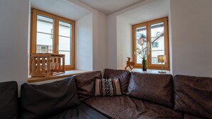 Ein Wohnzimmer mit braunem Ledersofa, einer Holzbank und einem Fenster mit Blick auf Gebäude.