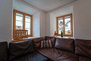 Ein Wohnzimmer mit braunem Ledersofa, einer Holzbank und einem Fenster mit Blick auf Gebäude.