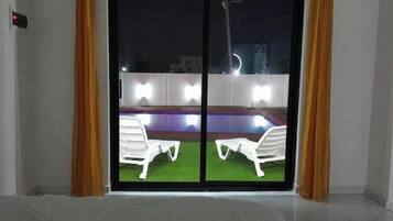 A room with a sliding glass door leading to an outdoor area with a pool and two white chairs.