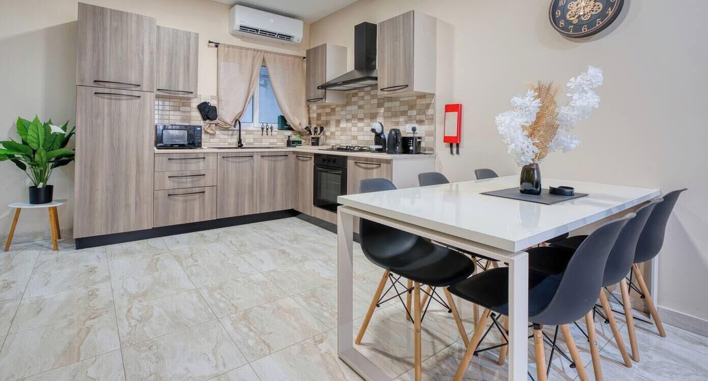 Une cuisine moderne avec un coin repas, comprenant une table blanche, des chaises noires et une plante en pot.