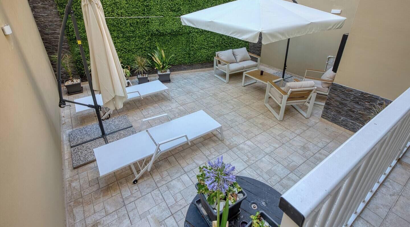 Une terrasse aménagée avec du mobilier d’extérieur, notamment un canapé, des fauteuils et une table, et un parasol blanc pour créer de l’ombre.