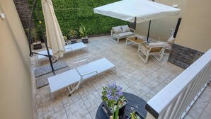 Une terrasse aménagée avec du mobilier d’extérieur, notamment un canapé, des fauteuils et une table, et un parasol blanc pour créer de l’ombre.