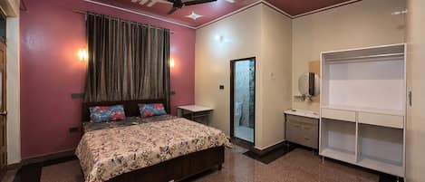 A bedroom with a bed, a ceiling fan, a nightstand, a small table, a mirror, and a wardrobe.