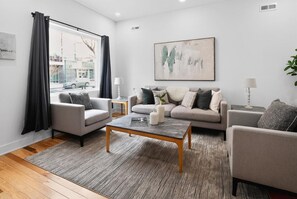 Un salon moderne avec un canapé, des fauteuils, une table basse et un grand tableau abstrait.
