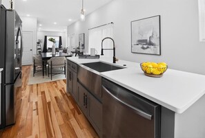 Une cuisine moderne avec un réfrigérateur en acier inoxydable, un plan de travail blanc et un évier.