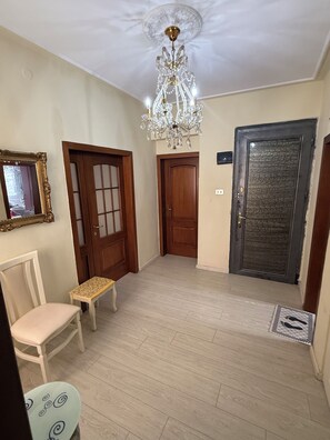 Un couloir orné d’un lustre, doté de portes en bois, d’un miroir et d’une chaise.