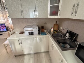 Eine Küche mit weißen Schränken, einem Spülbecken, einer Mikrowelle und einem Fernseher auf einem kleinen Tisch.