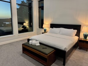 Ein Hotelzimmer mit einem großen Bett, einem Nachttisch mit Lampe, einem Fenster mit Blick ins Freie und einer kleinen Holzbank mit Handtüchern.