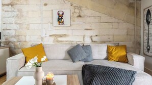 Una habitación con pared de ladrillo, un sofá a rayas con varios cojines, un jarrón con flores y una mesa con una vela.