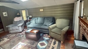 Ein Wohnzimmer mit hohen Decken, Oberlicht, einem gemusterten Teppich und einem Kamin.