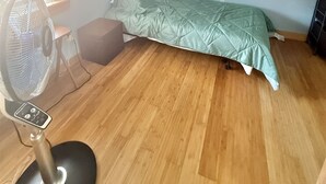 Eine kleine Einzimmerwohnung mit Bett, Standventilator, Tisch und Fenster.
