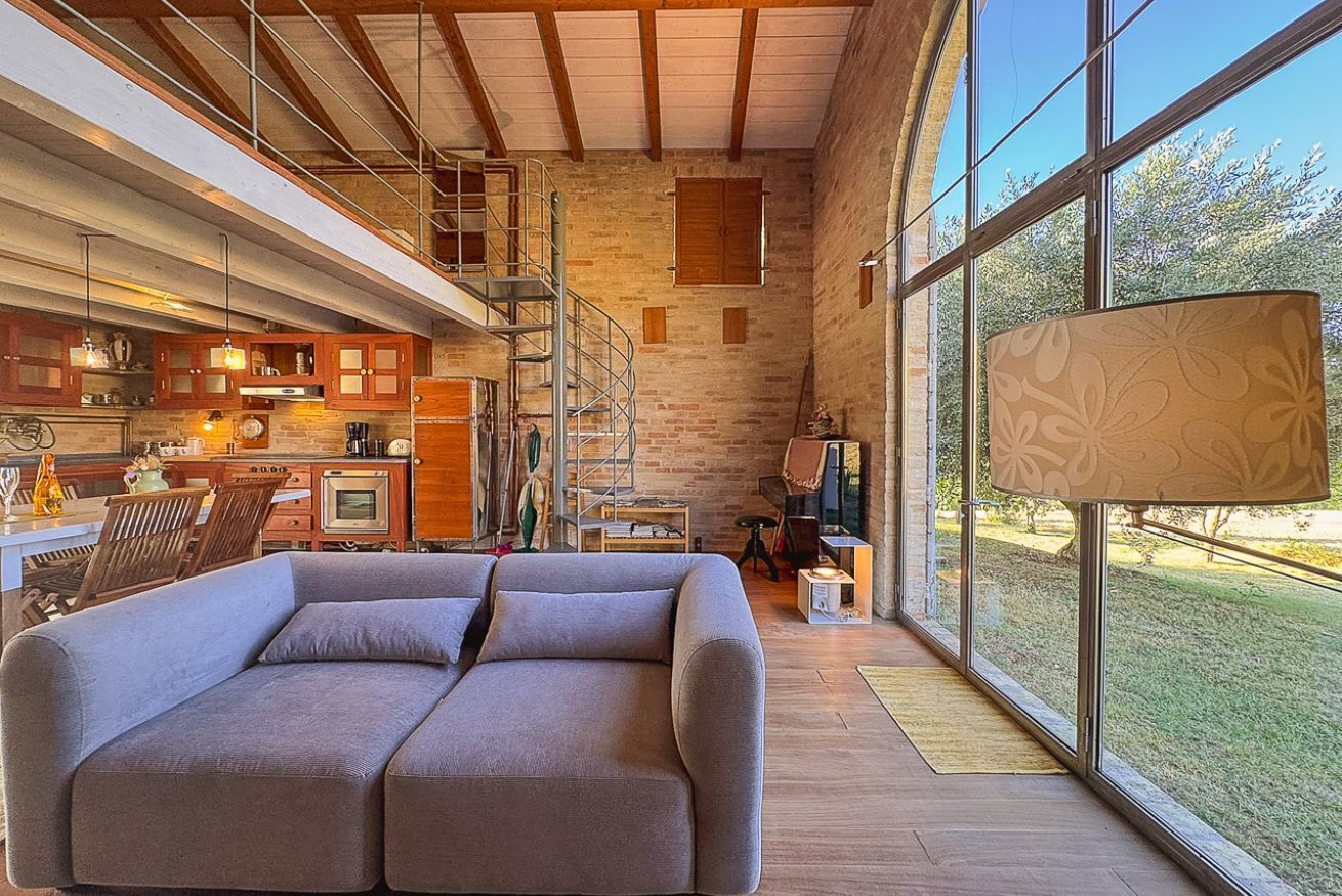 Un interno moderno con un divano, angolo cottura, scala e ampie finestre.