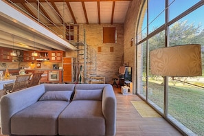 Un interno moderno con un divano, angolo cottura, scala e ampie finestre.