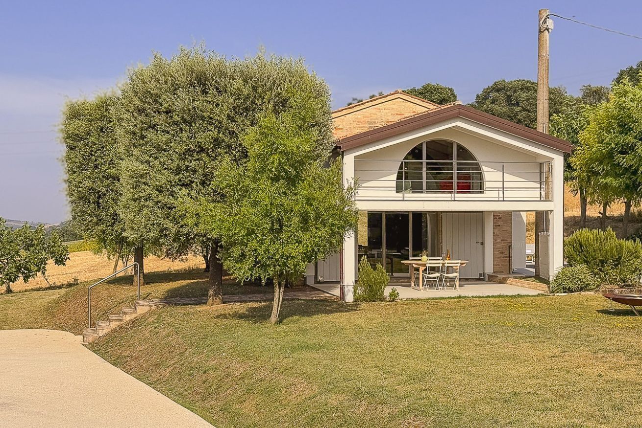 Una casa a un piano con una veranda coperta, un grande albero di fronte e cielo sereno.