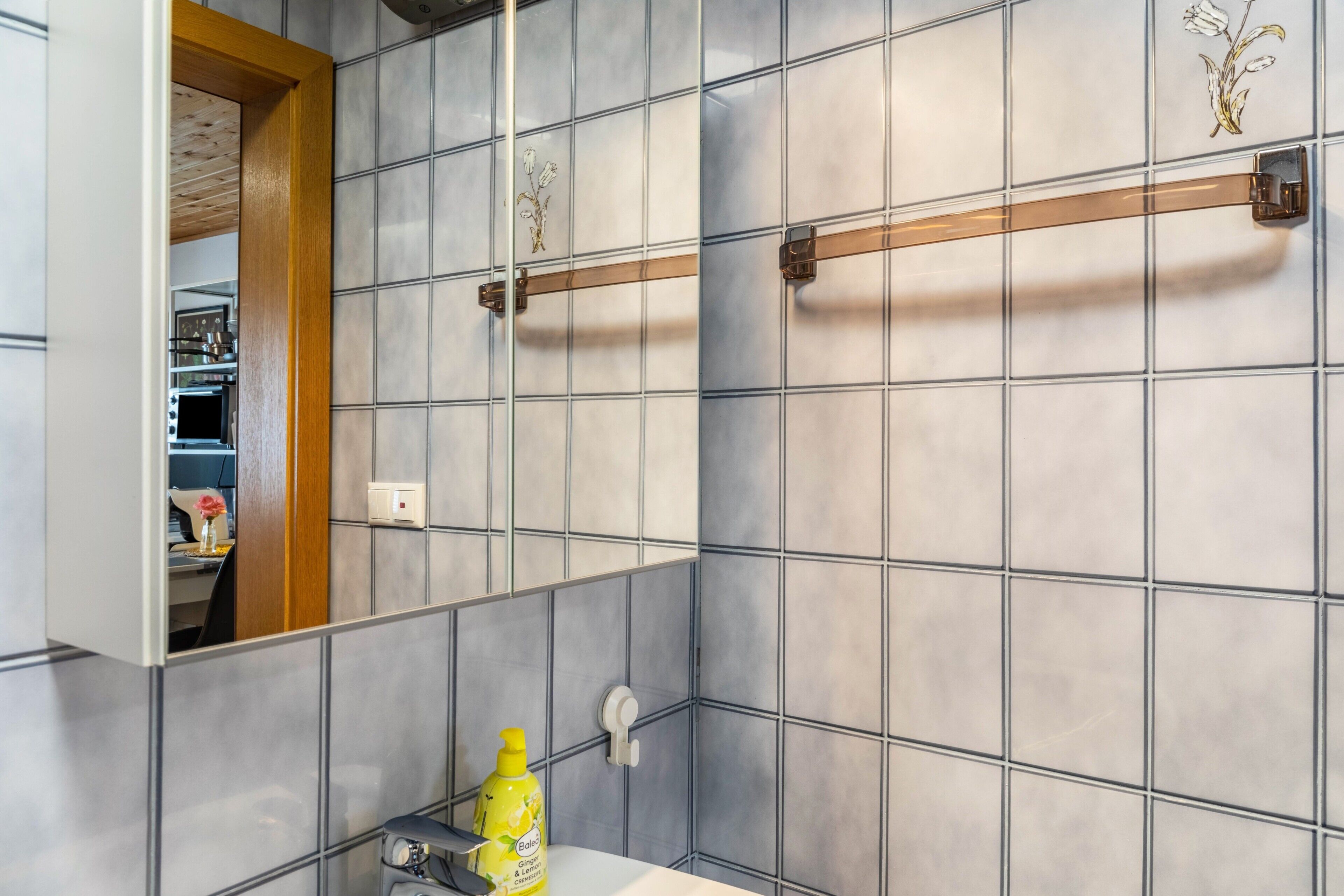 Ein Badezimmer mit einer gefliesten Wand, einem Holzrahmen, einem Spiegel, einem Waschbecken und einer Flasche Baled Zitrone-Ingwer-Creme.