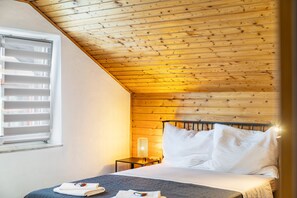 A bedroom with a sloped ceiling, a bed with white bedding, a bedside table with a lamp, and a window with blinds. - Studio-Apartment 'Lena 1 – Zentrale Lage mit Bergblick' (Bischofshofen)