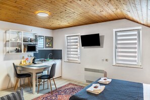 Una habitación compacta con kitchenette, una cama con toallas, televisión y ventana con persianas.