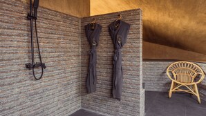 Zona de ducha con pared texturizada, bata colgada y silla de mimbre.