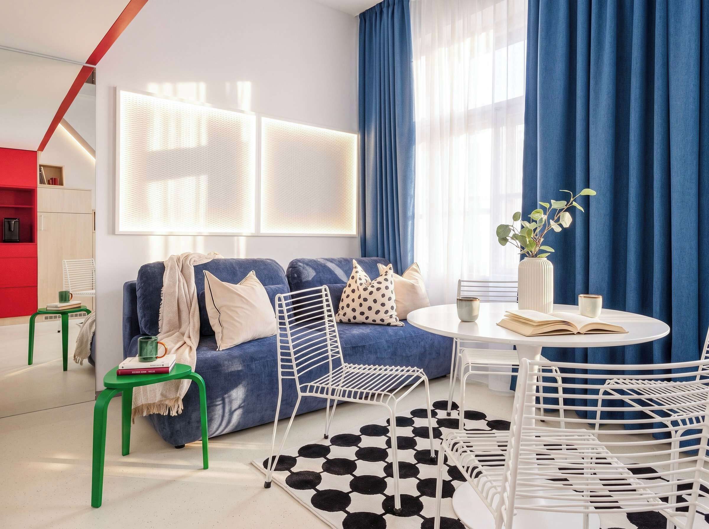 A modern living room with a blue sofa, white chairs, a round table, and a patterned rug.