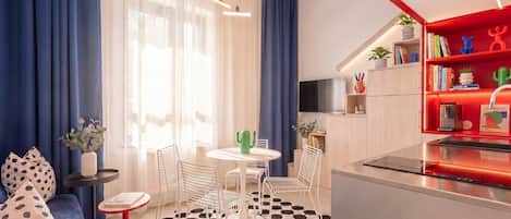 Un salon moderne avec un canapé, une table basse et des fauteuils, un coin cuisine avec une étagère rouge et un sol à carreaux noirs et blancs.
