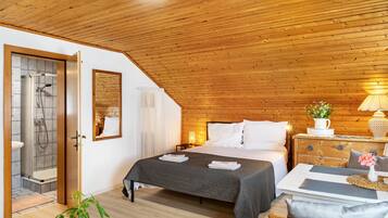 Een gezellige slaapkamer met een houten plafond, een bed met witte lakens, een nachtkastje met een lamp, en uitzicht op een badkamer met douche.