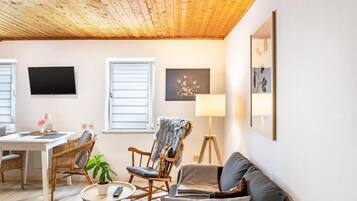 Ein gemütliches Wohnzimmer mit Holzboden, einem Fernseher, einem Sofa, einem Sessel, einer Stehlampe und einem Bild an der Wand.