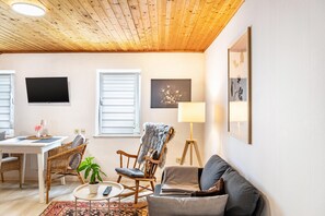 A cozy living room with a wooden ceiling, a television, a sofa, a chair, a floor lamp, and a painting on the wall.