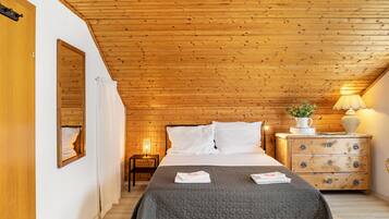 A bedroom with a wooden ceiling, a bed with white bedding, a nightstand with a lamp, and a dresser with drawers.