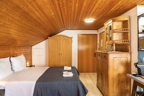 Ein Schlafzimmer mit Holzboden, einem Bett mit gesteppter Bettdecke, einem Holzschrank und einem kleinen Tisch mit Lampe.