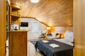 A cozy attic bedroom with a wooden ceiling, a bed with a quilted cover, a chair, a small table, and a television mounted on the wall. - Studio-Apartment 'Lena Apartments 3' (Bischofshofen)