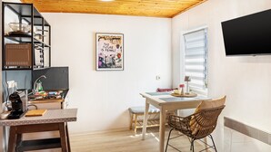 Et kompakt køkken med træloft, et spiseområde med bord og stole, samt et vægmonteret tv.