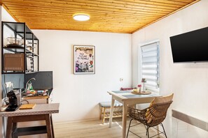 A compact kitchen with a wooden ceiling, a dining area with a table and chairs, and a wall-mounted TV. - Studio Apartment Lena Apartments 3 (Bischofshofen)